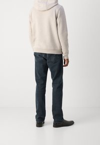 Sudadera gris clara con capucha, combinada con jeans azul oscuro. Los jeans tienen un diseño clásico de cinco bolsillos y un corte recto. Zapatos negros visibles.