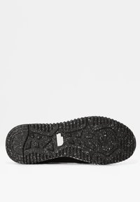 Semelle de chaussure noire mouchetée avec des crampons profonds et un petit logo blanc North Face au centre.
