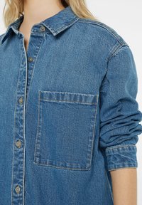 Denim shirt with a classic collar, Front button closure, long sleeves, a single chest pocket, and visible stitching in contrasting color.