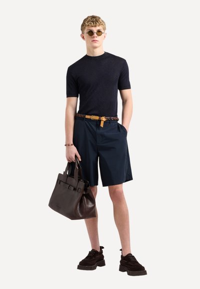 Maglietta nera a maniche corte con texture, pantaloni corti blu scuro, cintura in pelle marrone, borsa a spalla marrone e scarpe scure con suola spessa.