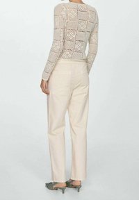 Lehký pletený béžový svetr s mřížkovým vzorem, sladěný s krémovými kalhotami a zelenými sandály na podpatku. Viditelný design na zadní straně a kapsy.