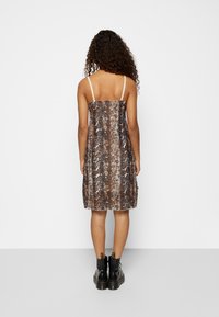 Šaty se vzorem hada v hnědých a béžových odstínech, s tenkými ramínky, ve tvaru A, končící nad koleny, v kombinaci s černými šněrovacími botami.