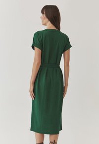 Groene jurk tot de knie met korte mouwen en een ceintuur in de taille, gemaakt van een gestructureerde stof. Beschikt over een eenvoudig ontwerp en zijsplitten.