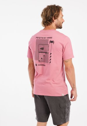 T-shirt in cotone rosa con una stampa grafica sul retro caratterizzata da linee nere e forme geometriche, abbinata a pantaloni cargo grigi.