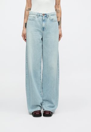 Jean large couleur bleu clair en denim. Comprend une fermeture à boutons, des poches avant, et une finition délavée. Associé à des chaussures à plateforme foncées.