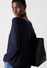 Marineblå strikkegenser med vid utringning, lange ermer og teksturert stoff. Kombinert med en svart skinn totebag. Enkel bakdetalj.