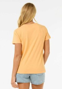 Korte mouwen, ronde hals T-shirt van zacht, perzikkleurig katoen. Eenvoudig ontwerp met een ontspannen pasvorm, gedragen met lichtblauwe denim shorts.