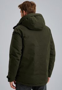 Zelená kapuce s hladkou strukturou a prošívaným designem. Obsahuje ramenní nášivku a volný střih, který sahá k bokům.