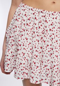 Gonna a balze floreale realizzata in tessuto leggero, con piccoli fiori rossi su sfondo bianco, dotata di una fascia in vita elastica arricciata.