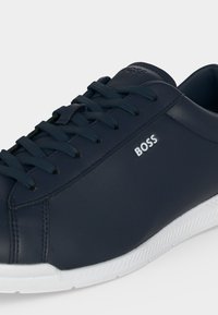 Baskets en cuir bleu marine avec lacets noirs, semelle blanche texturée et logo "BOSS" sur le côté, présentées en gros plan.