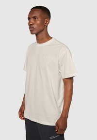 Kortærmet, cremefarvet bomulds T-shirt med rund hals og lille broderet logo på brystet. Glat tekstur, afslappet pasform.