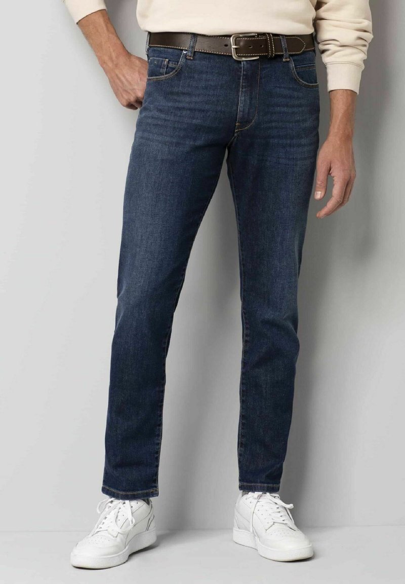 Donkerblauwe denim jeans met een rechte pasvorm, voorzien van vijf zakken, een bruine leren riem en witte sneakers voor contrast.