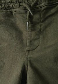 Pantaloni verde oliva con cintura elastica e cordoncino regolabile. Texture liscia e dettagli di cucitura visibili lungo le cuciture.