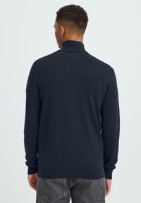 Tengerészkék pulóver magas gallérral, hosszú ujjakkal, bordázott mandzsettával és szegéllyel. Puha, texturált anyagból készült.