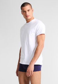 Witte katoenen t-shirt met korte mouwen, eenvoudige uitstraling, ronde hals, gedragen met marineblauwe korte broek. Eenvoudige, getailleerde vorm, gladde textuur.