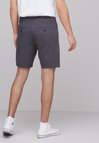 Shorts gris en tissu léger, dotés de deux poches arrière avec boutons et d'une coupe droite, associés à des baskets montantes blanches.