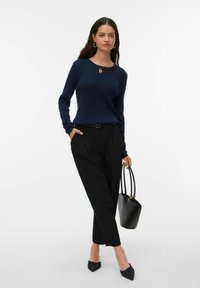 Pull côtelé bleu marine à manches longues associé à un pantalon noir taille haute. Les accessoires comprennent des boucles d'oreilles créoles et un sac à main noir avec des accents dorés.