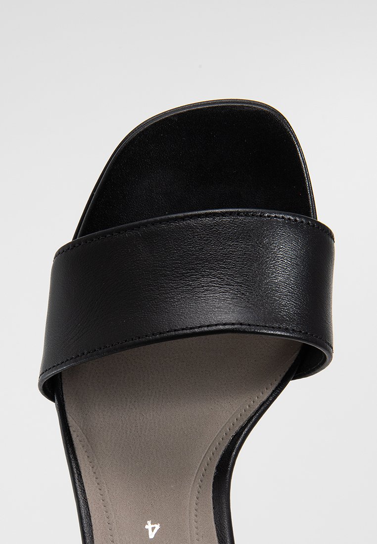 Sandale noire à glissière avec une large bride en cuir et une semelle intérieure lisse et rembourrée. Le design est minimaliste avec une forme de orteil arrondie.