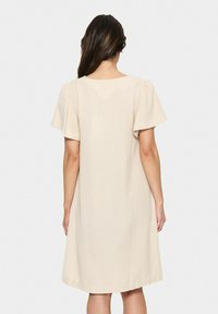 Beiges, kurzärmeliges Kleid mit lockerer Passform, runder Halslinie und weicher Textur, das über dem Knie endet. Einfaches und minimalistisches Design.