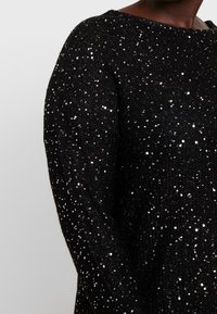 Maglione nero con paillettes caratterizzato da una vestibilità ampia, scollo rotondo e tessuto a maglia testurizzato, decorato con numerose paillettes scintillanti.