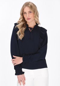 Blusa blu navy con dettagli arricciati, scollatura con fiocco e polsini arr gathered. Tessuto morbido con una finitura liscia, adatta per un abbigliamento casual o formale.