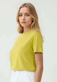 T-shirt verde lime a maniche corte, scollatura rotonda, tessuto morbido, vestibilità aderente, abbinato a pantaloni bianchi a vita alta. Design semplice, senza fantasie.