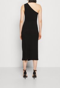 Czarna sukienka na jedno ramię o dopasowanej sylwetce, do kolan, z miękkiej tkaniny. Noszona z czarnymi szpilkami.