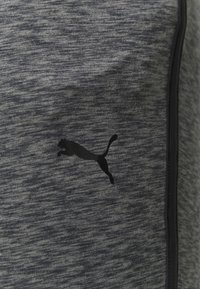 Tejido gris oscuro con un logo negro de Puma que representa a un puma saltando y ribetes verticales negros en el lado derecho.