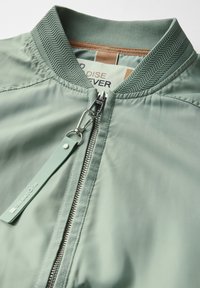 Světle zelená bomber bunda s vroubkovaným límcem, předním zipem s kovovým kováním a látkovou visačkou s nápisem "Street One."