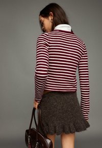 Gestreepte bordeauxrode en witte trui met een cropped ontwerp, gecombineerd met een grijze textuurrijke rok met een gerimpelde zoom. Bruine handtas in de hand gehouden.