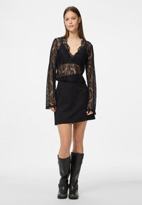 Crna čipkana kratka majica s dugim rukavima i V-izrezom, uparena s crnom mini suknjom. Nosena s crnim kožnim čizmama do koljena.