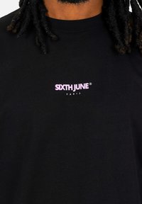 Camiseta de algodón negra con un pequeño logo impreso en rosa "SIXTH JUNE PARIS" en la parte delantera, cuello redondo y mangas cortas.