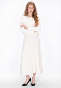 Pulover alb tricotat, scurt, cu mâneci lungi, asociat cu o fustă lungă albă și pantofi cu toc înalt negri. Design simplu și elegant.