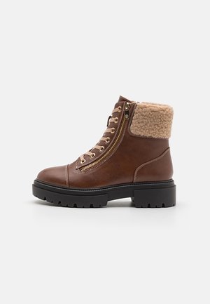 Bottine en cuir marron avec semelle noire épaisse, fermeture éclair latérale, laçage à l'avant et doublure en polaire beige au niveau du col, sur fond uni.