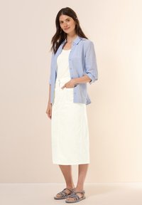Lyseblå button-up skjorte, hvid tanktop, hvid midi-nederdel med lommer og grå strap sandaler, sat op mod en neutral baggrund.
