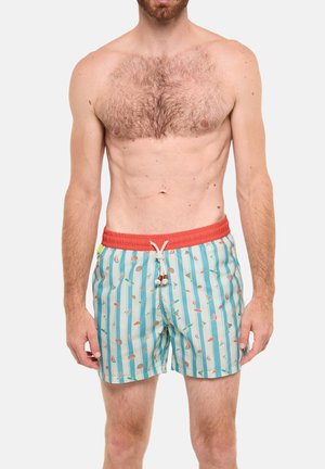 Homme torse nu portant un short de bain bleu clair à rayures verticales et motif plage, avec une ceinture rouge et un cordon blanc avec des perles en bois.