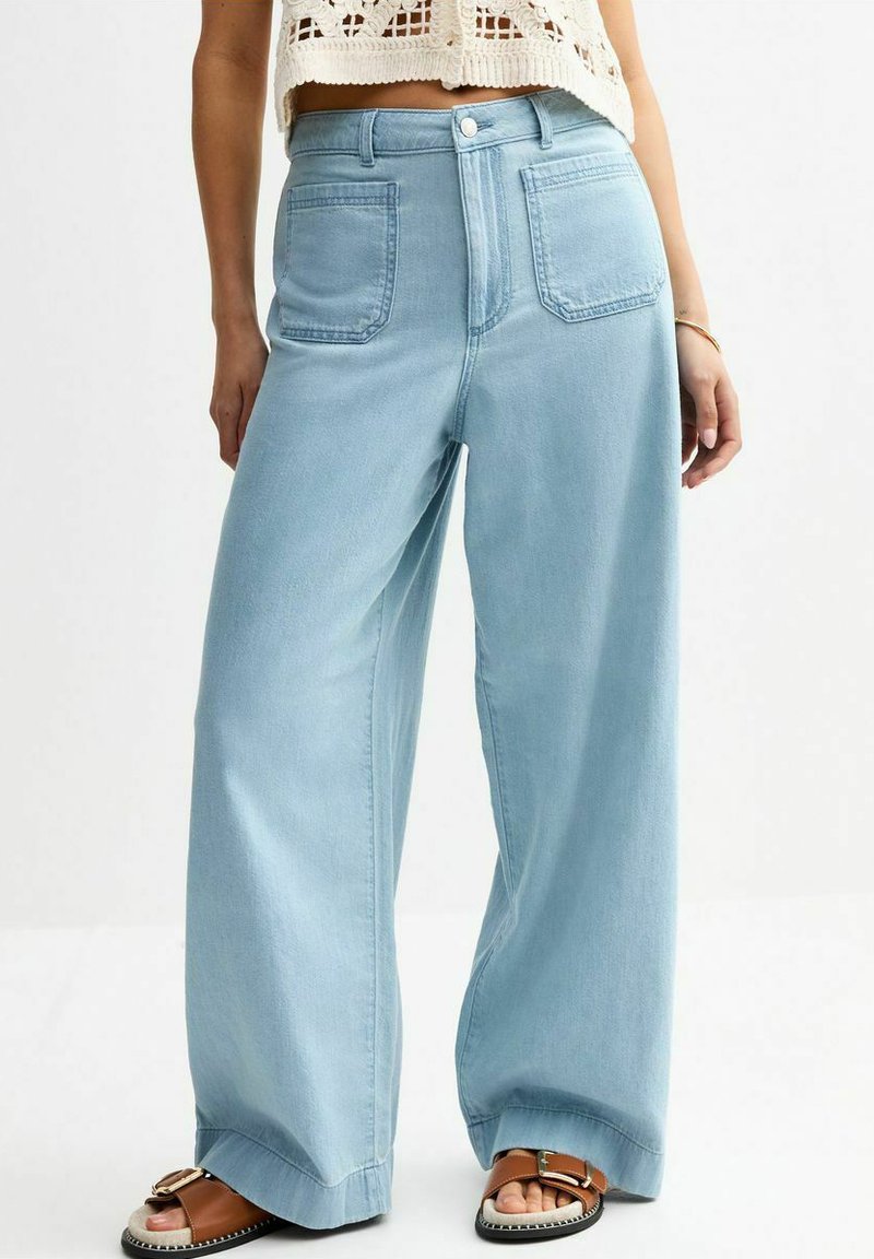 Pantalones vaqueros de pierna ancha en azul claro con una cintura alta, que cuentan con bolsillos delanteros y traseros y un cierre de botón discreto. Textura de denim suave.