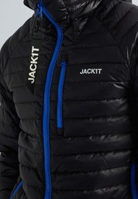 Veste noire matelassée avec des fermetures éclair et des accents bleus. Comprend une étiquette de marque et une poche zippée sur la poitrine gauche. Surface extérieure texturée.