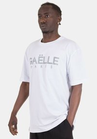 T-shirt bianco in cotone con logo "GAËLLE PARIS" in borchie argentate, vestibilità rilassata con maniche corte e scollatura rotonda.