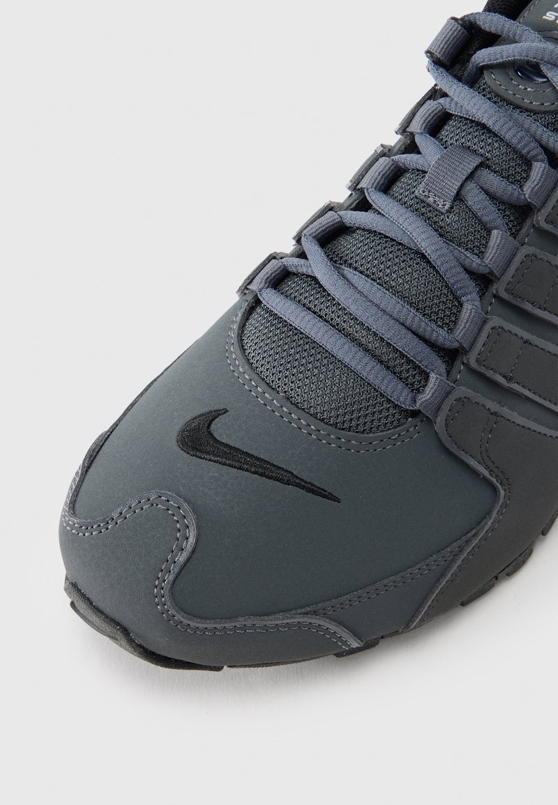 Gray athletic shoe with textured upper and mesh accents. Features dark gray laces and a black Nike swoosh logo on the toe area.