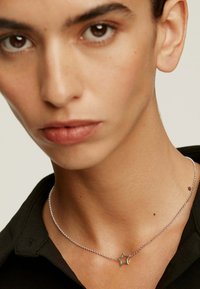 Collar de cadena de plata con un colgante en forma de estrella, llevado sobre piel desnuda, con una textura suave y un diseño minimalista, contra una camisa negra.