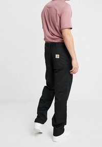 Czarne spodnie robocze o luźnym kroju, z tylną naszywką z logo i bocznymi kieszeniami, zestawione z różowym T-shirtem z okrągłym dekoltem i białymi trampkami.