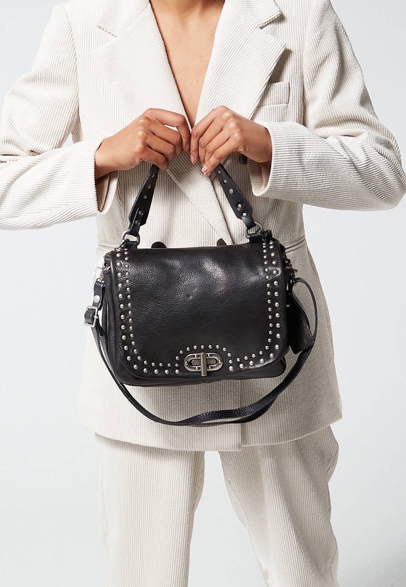 Borsa a tracolla in pelle nera con dettagli borchiati argentati, chiusura a patta e tracolle regolabili. Presenta un logo decorativo sulla parte frontale.