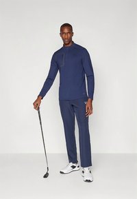 Tumesinise golfiriietus, mis koosneb pika varrukaga särgist kvartstõmblukuga ja kontrastse õmblusega, mida kannavad sobivad püksid ja valged spordijalatsid.