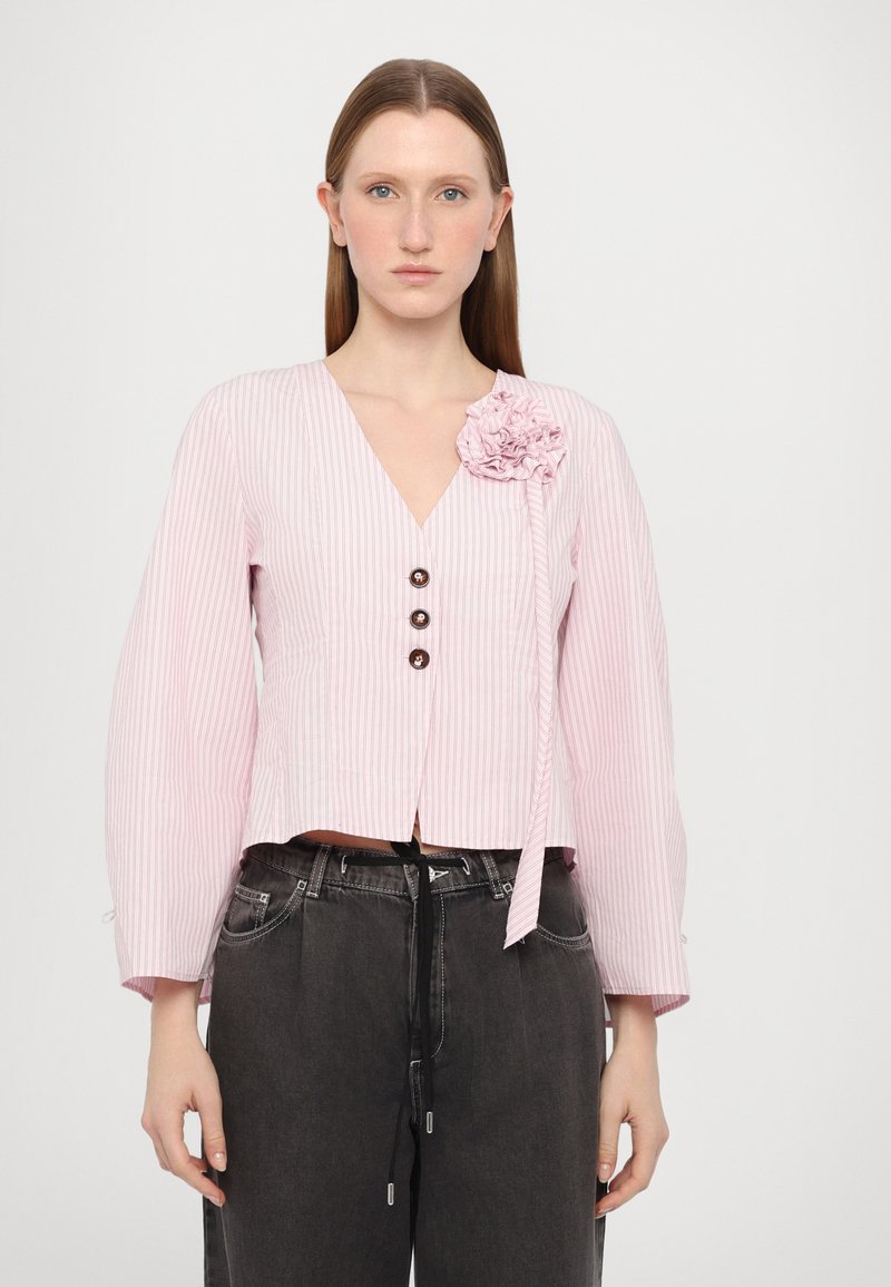 Blusa a righe verticali di un rosa chiaro, con scollatura a V, maniche lunghe, tre bottoni marroni e un dettaglio floreale testurizzato sulla spalla.