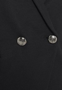 Černá dvouřadá sako s texturovanou látkou a dvěma kovovými knoflíky s propracovanými kruhovými vzory.