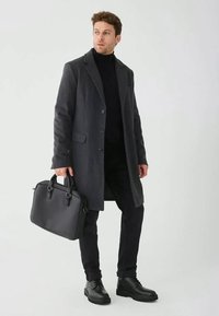 Dunkler Wollmantel mit taillierter Passform, Knopfleiste und eingestanzten Revers. Schwarzer Rollkragenpullover und Hose. Schwarze Lederaktentasche mit zwei Griffen.