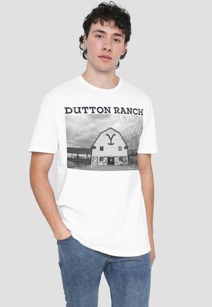 White cotton t-shirt featuring a black-and-white barn graphic with the text "DUTTON RANCH Since 1886." Simple crew neckline and relaxed fit.