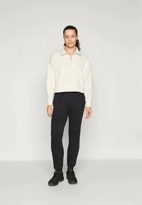 Cream fleece pullover with a quarter zip, paired with black fitted pants and black sneakers, set against a plain light background.