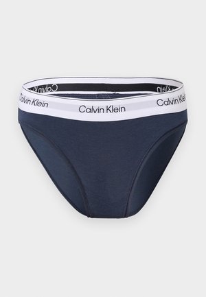Donkerblauwe Calvin Klein slip met witte elastische tailleband met zwarte Calvin Klein logo-tekst.